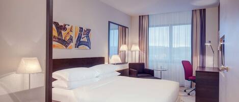 A hotel room with a large bed, a desk, two chairs, and artwork on the wall.