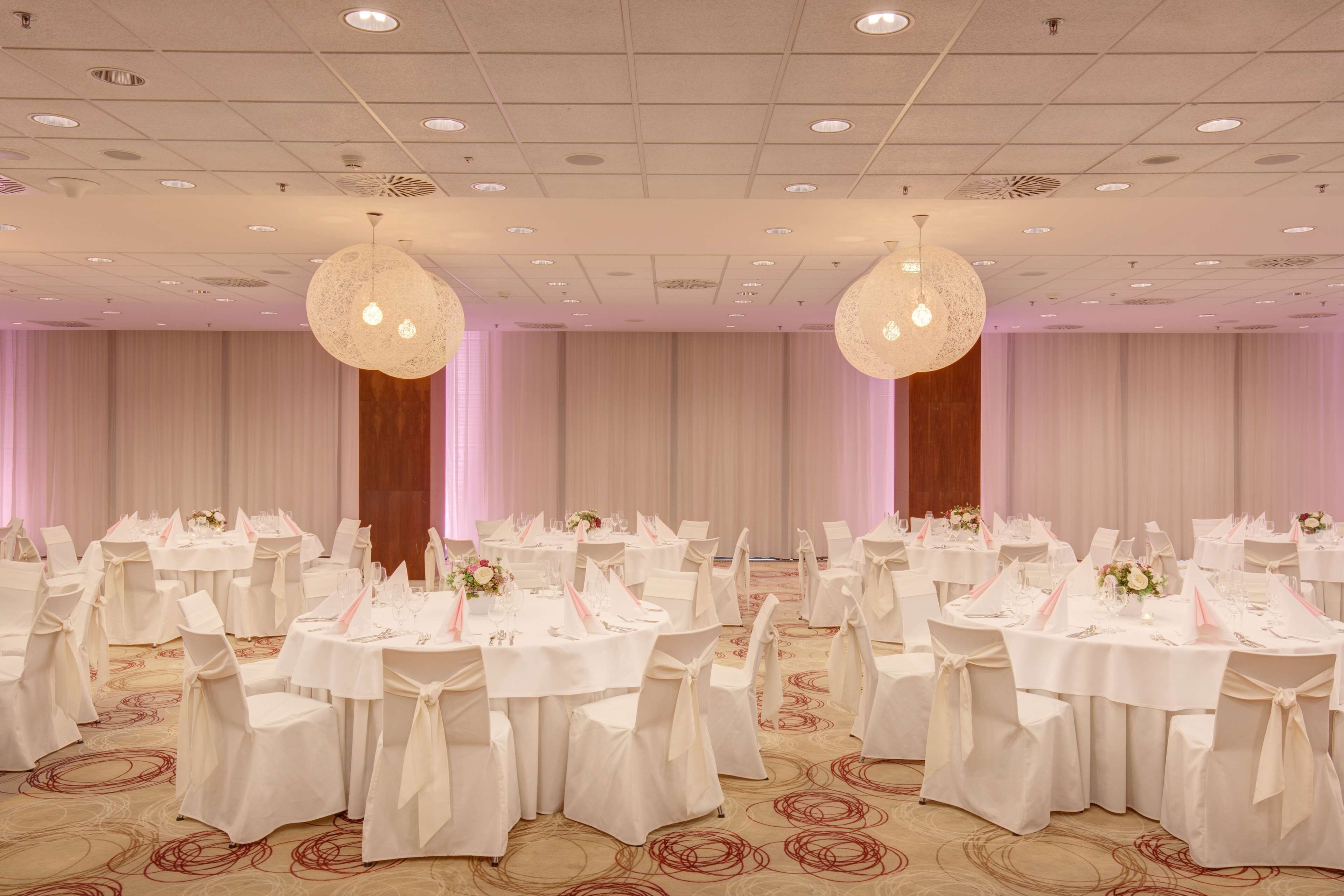 Un salón de banquetes con mesas redondas, manteles blancos y sillas con fundas blancas.