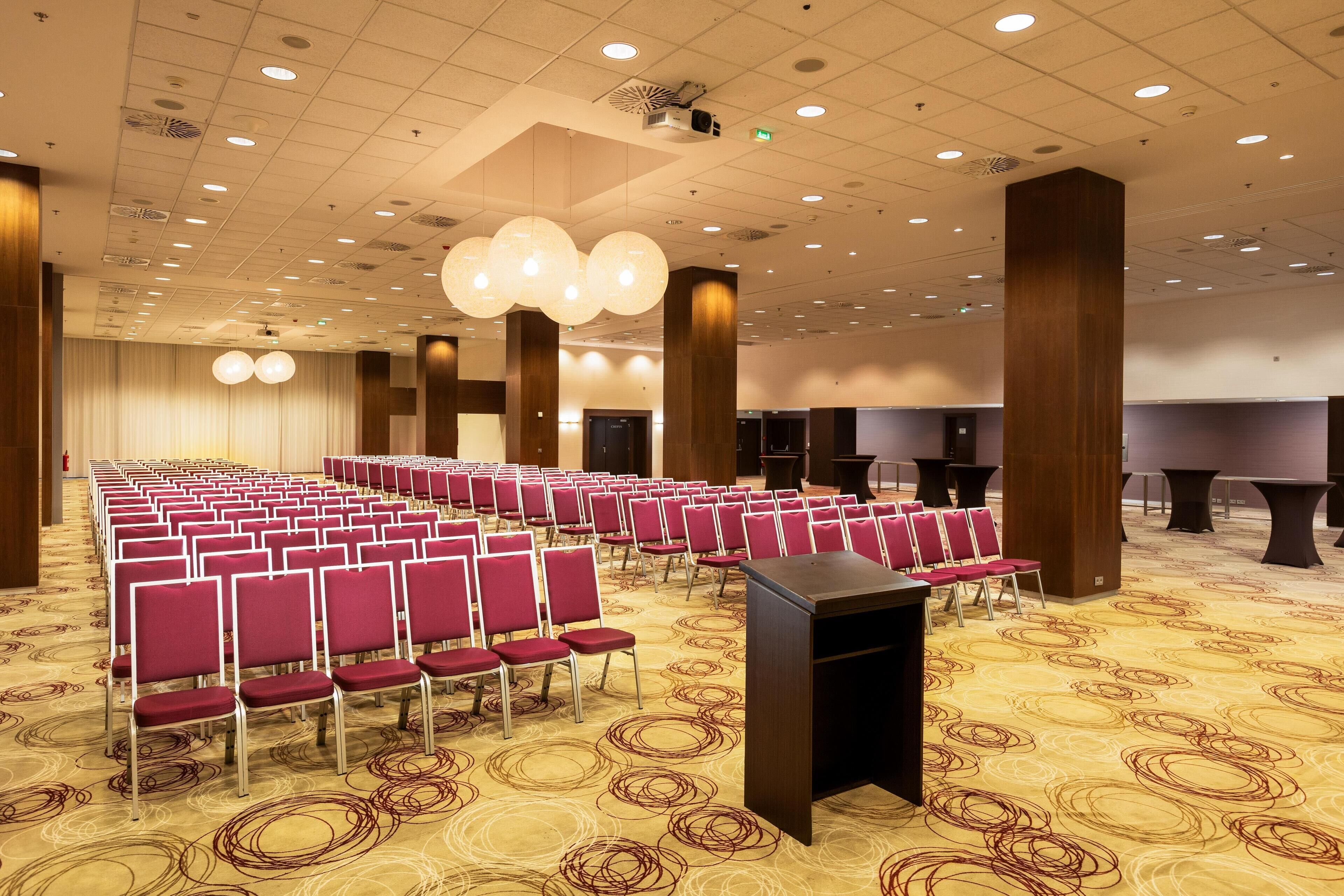 Un salón de conferencias con filas de sillas, un atril y suelo alfombrado.