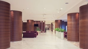 A modern lobby with marble flooring, large wooden columns, and seating areas.