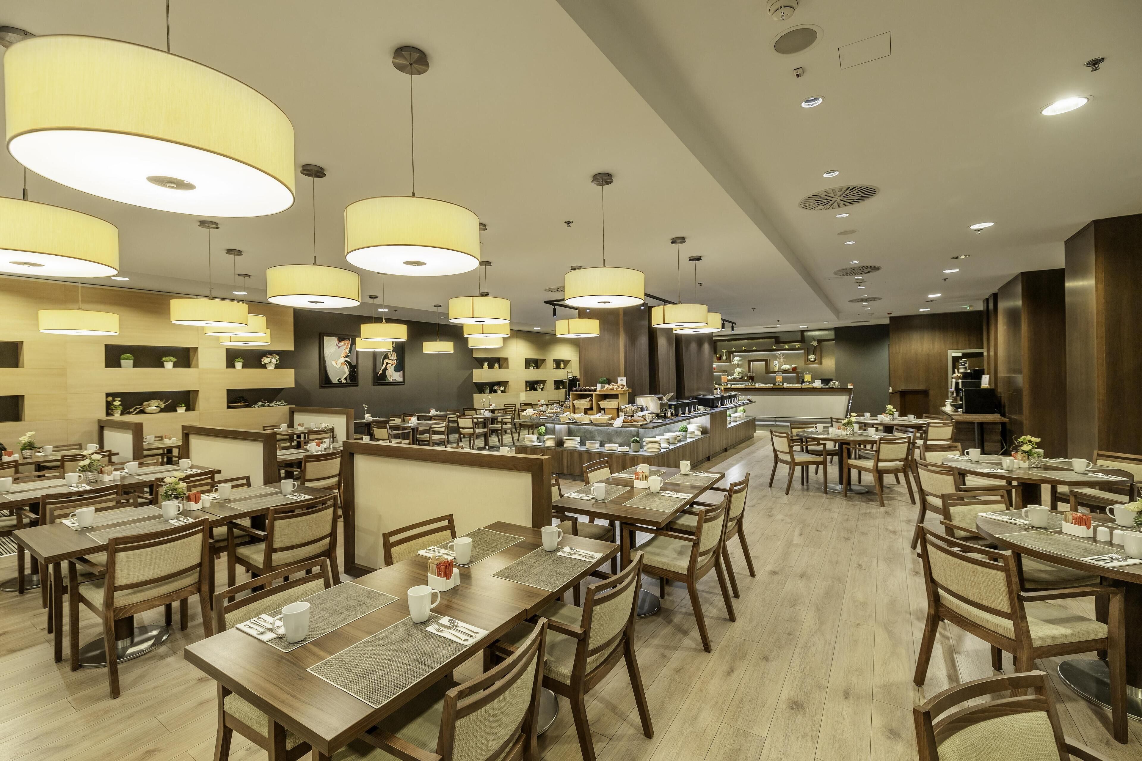 Un restaurante espacioso con varias mesas y sillas, grandes lámparas colgantes y un diseño interior moderno.