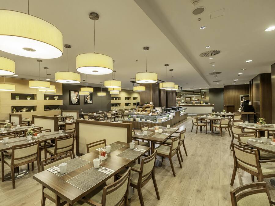 Un restaurante espacioso con varias mesas y sillas, grandes lámparas colgantes y un diseño interior moderno.