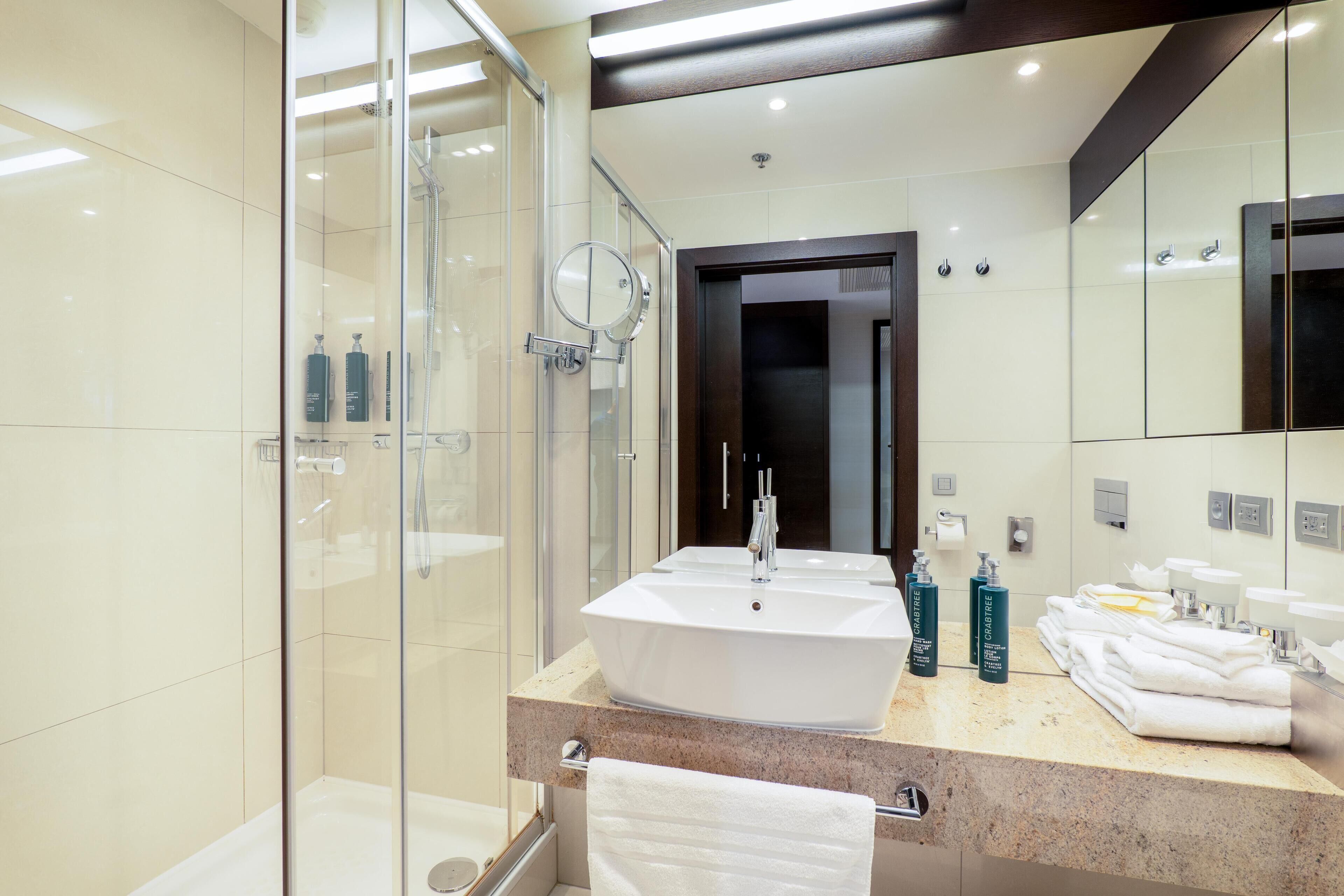 Un baño moderno con ducha de vidrio, un lavamanos amplio con espejo y artículos de aseo ordenados.