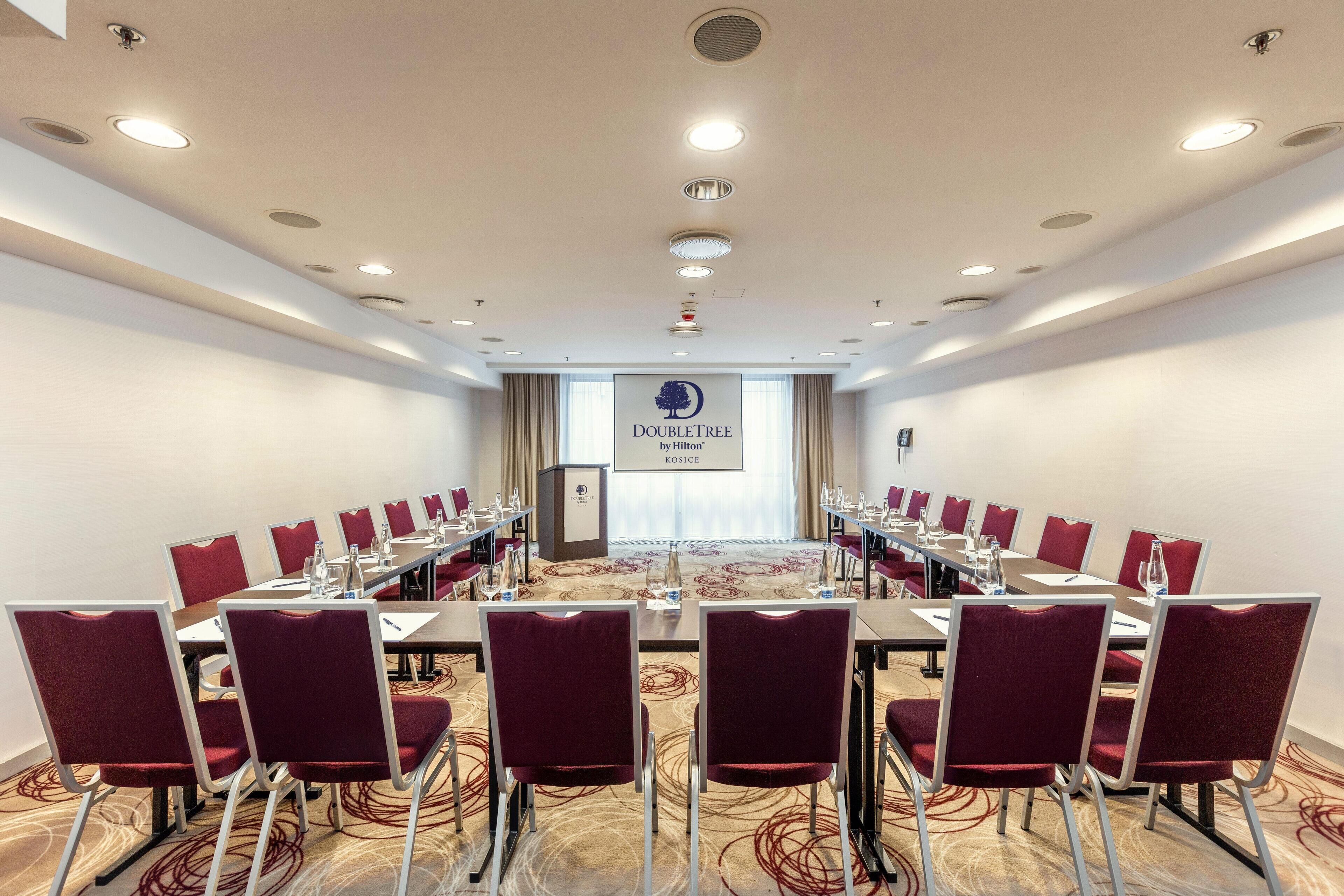 A conference room with a long table, red chairs, and a podium.