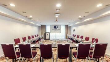 Un salón de conferencias con una larga mesa, sillas rojas y un atril.