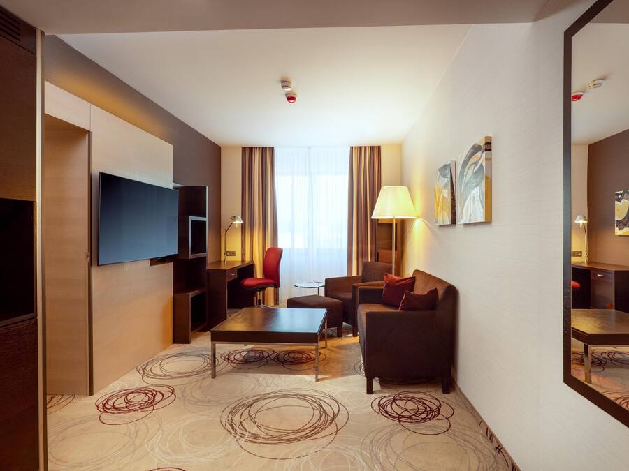 Ein Hotelzimmer mit Flachbildfernseher, Sofa, Couchtisch, Lampe und einem großen Spiegel.