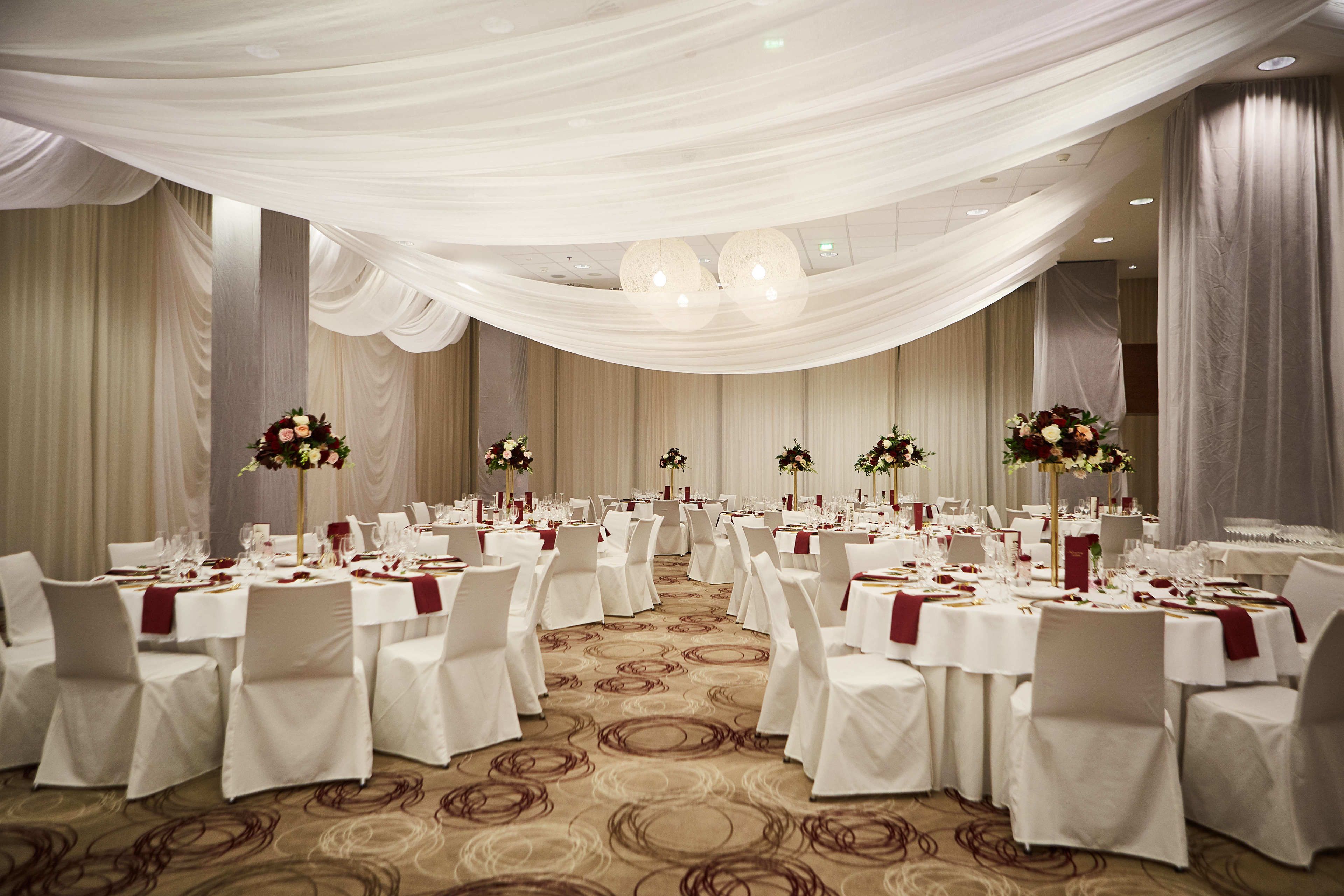 A banquet hall with round tables, white tablecloths, and red napkins.