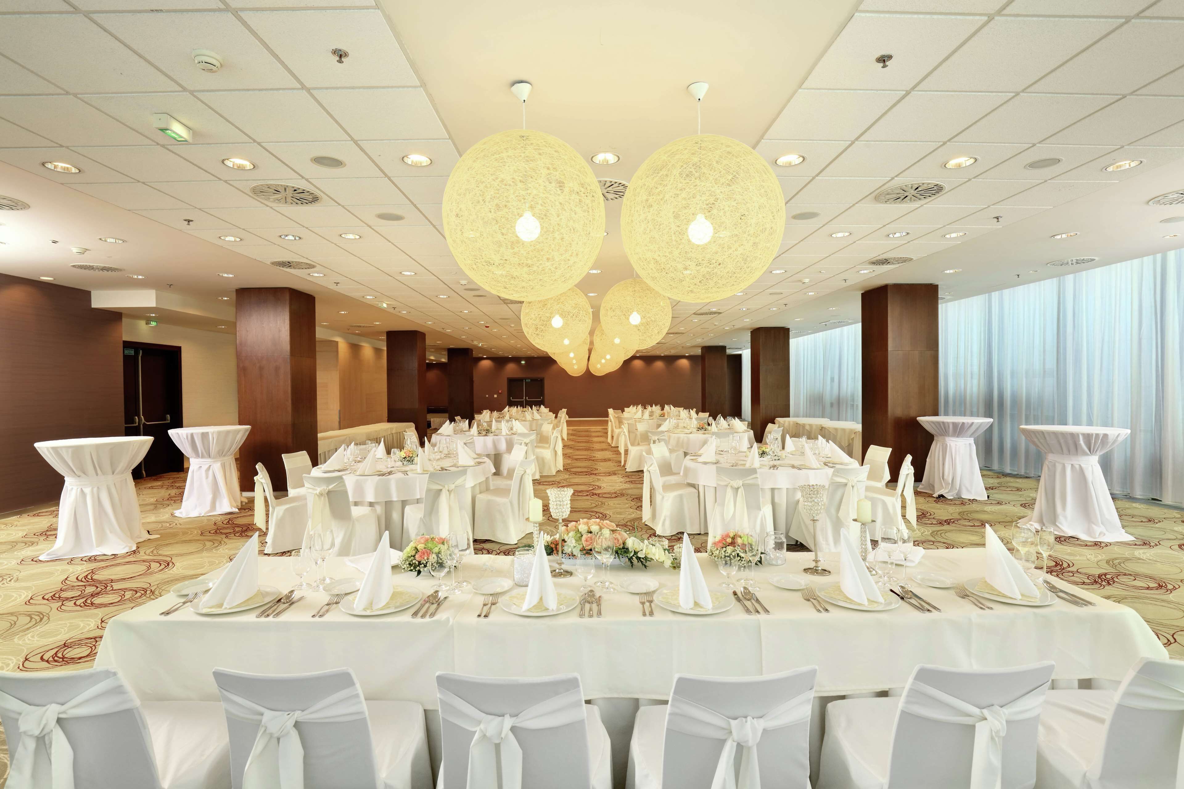 Une salle de banquet avec des tables rondes dressées pour un événement formel, agrémentée de nappes blanches, de chaises et de compositions florales.