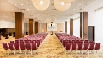 Un salón de conferencias con hileras de sillas rojas, un atril y una pantalla que muestra “DOUBLETREE by Hilton KOSICE”.