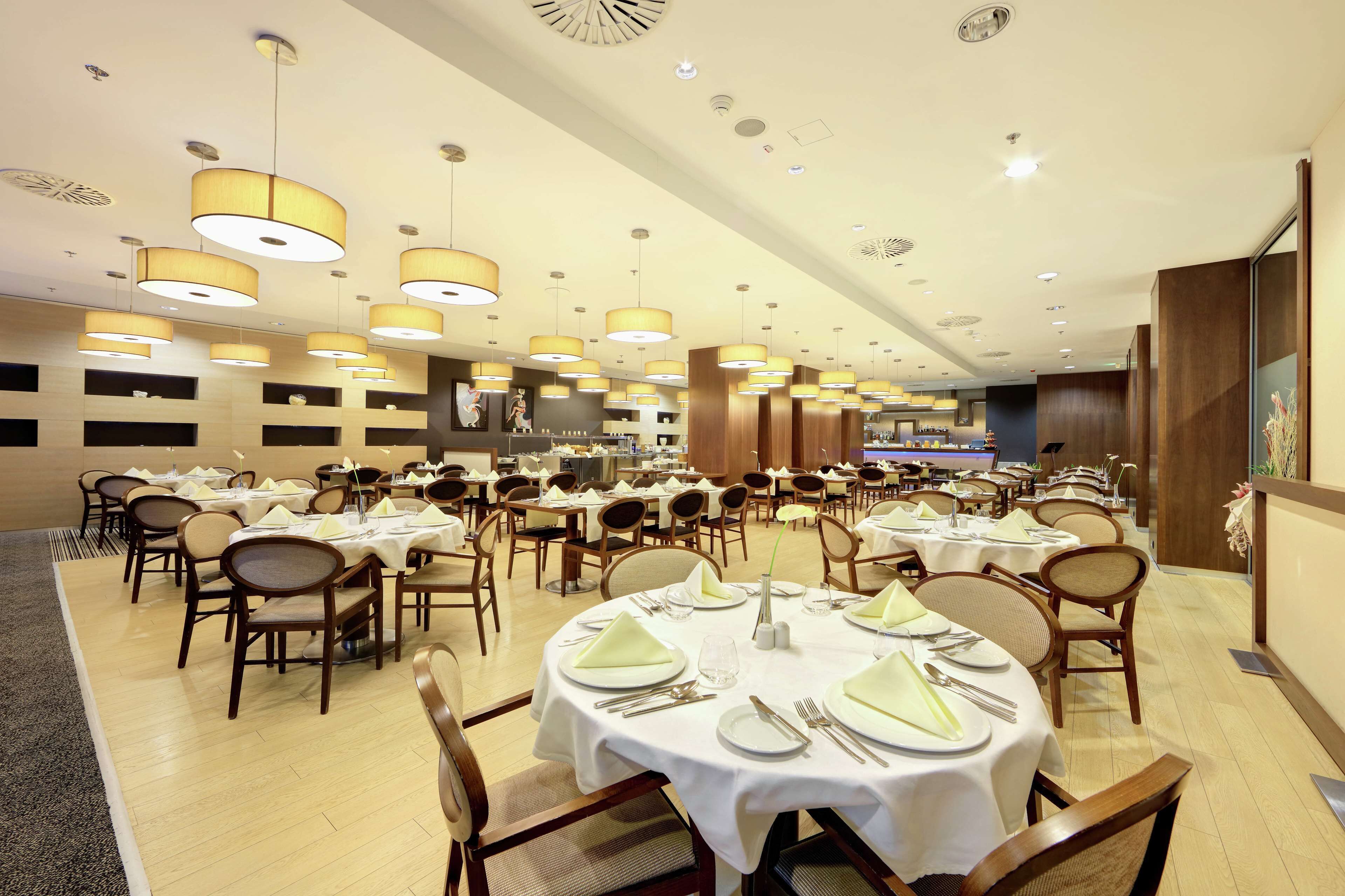 Un comedor amplio con varias mesas redondas dispuestas para comer, cada una con manteles blancos y cubertería ordenada.