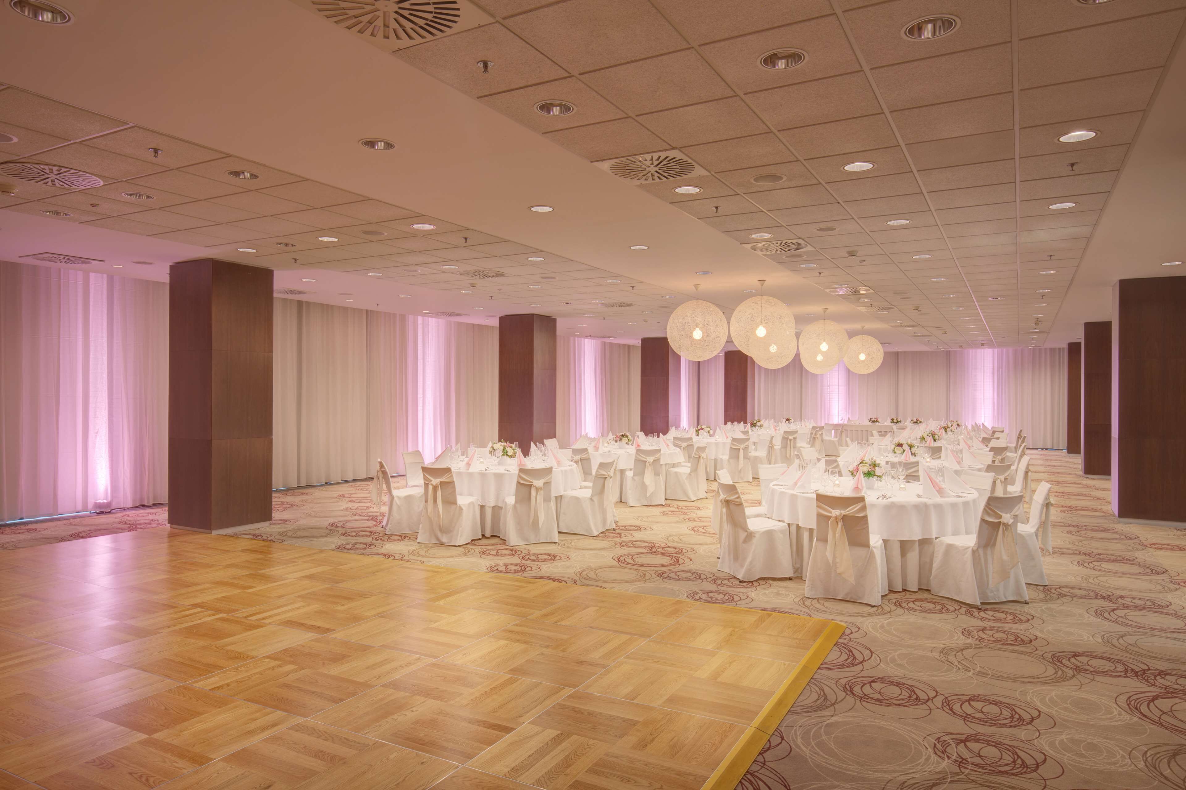 A spacious hall with round tables and chairs, a wooden floor, and a patterned carpet.