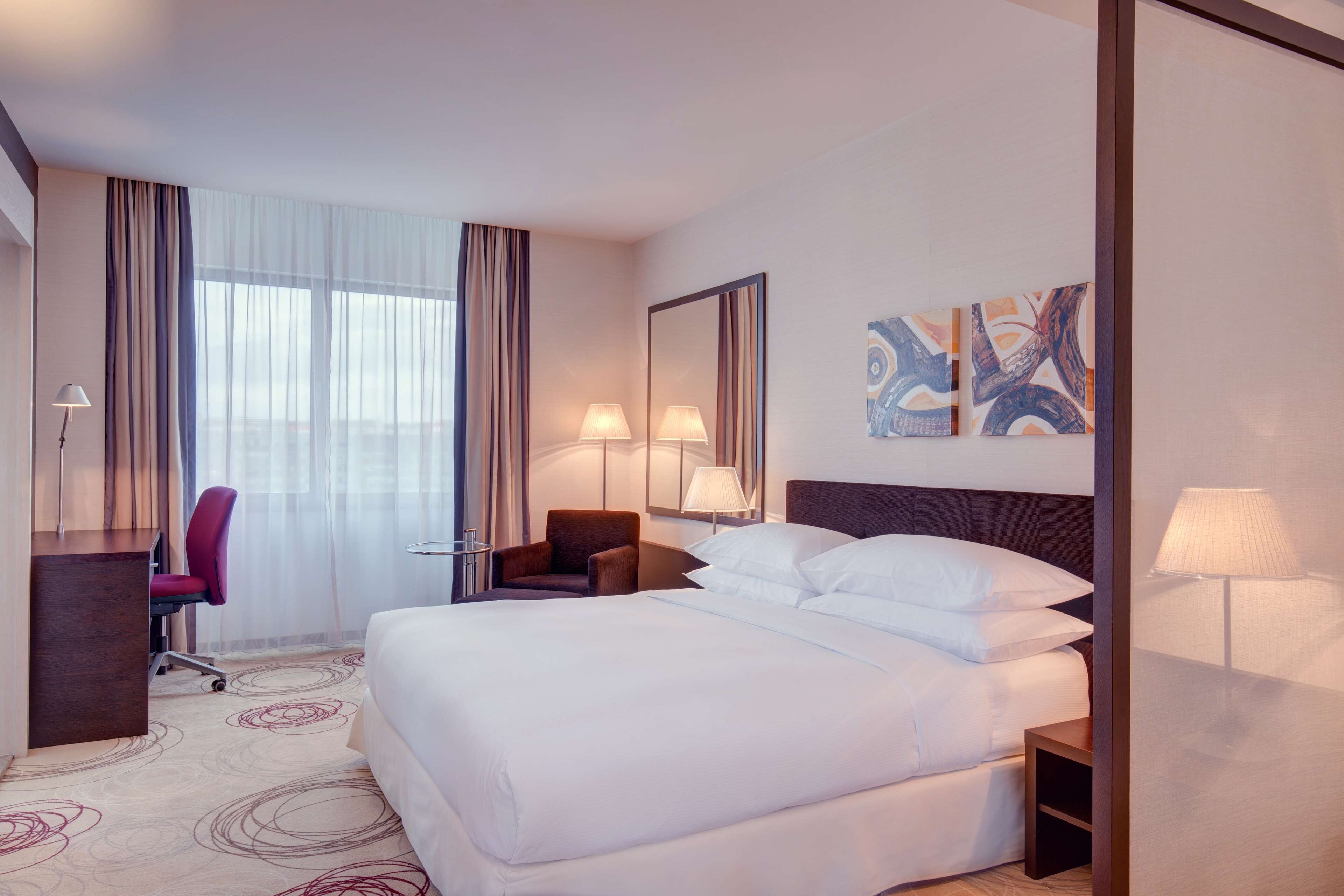 Een hotelkamer met een groot bed, een bureau, een stoel en een raam met gordijnen.