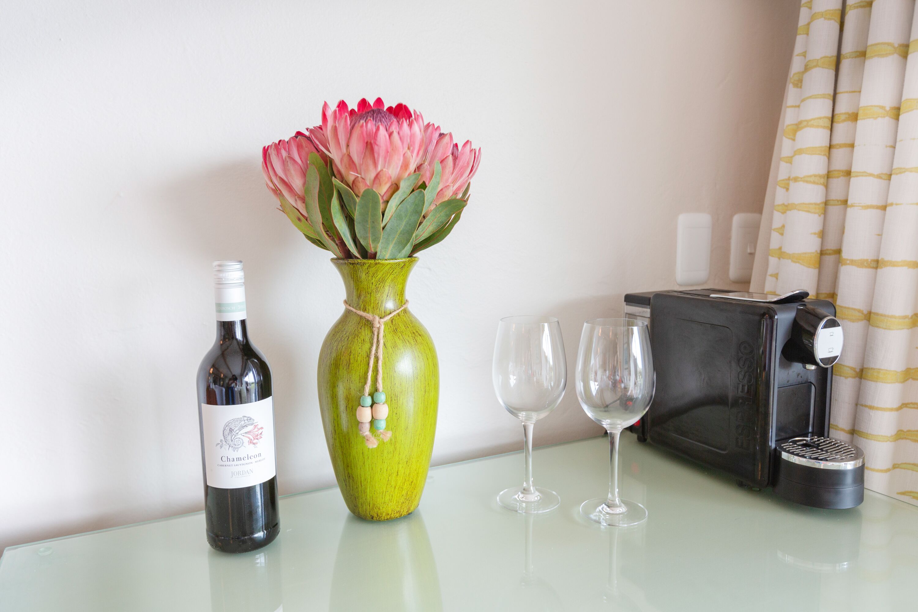 A table with a wine bottle, a vase with flowers, two wine glasses, and a coffee maker.