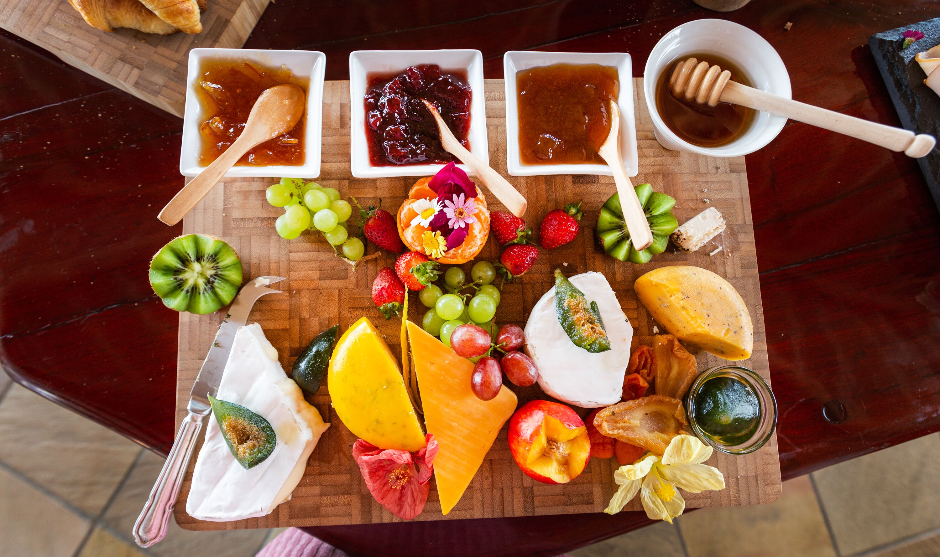 A charcuterie board with various cheeses, fruits, and jams.