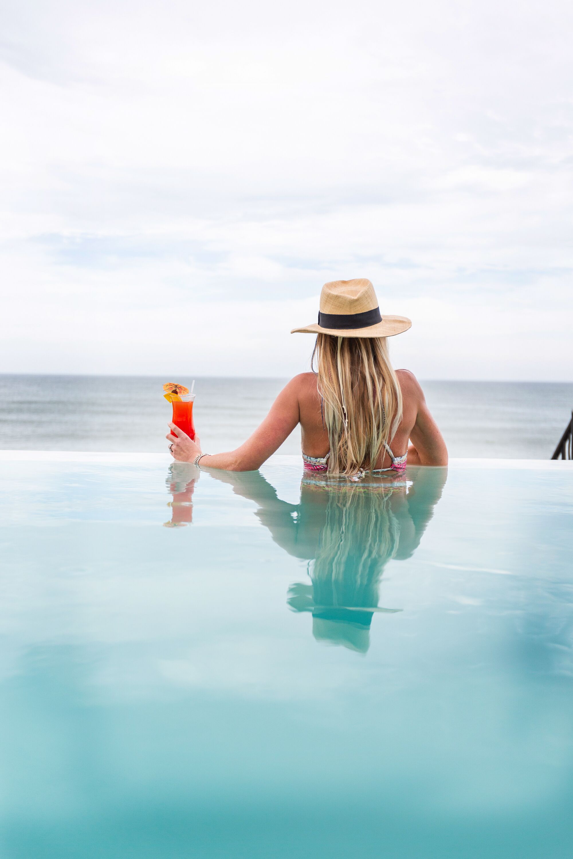 Eine Person sitzt an einem Glastisch am Meer und hält ein Getränk.