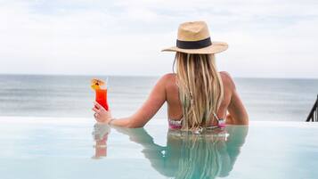Eine Person sitzt an einem Glastisch am Meer und hält ein Getränk.
