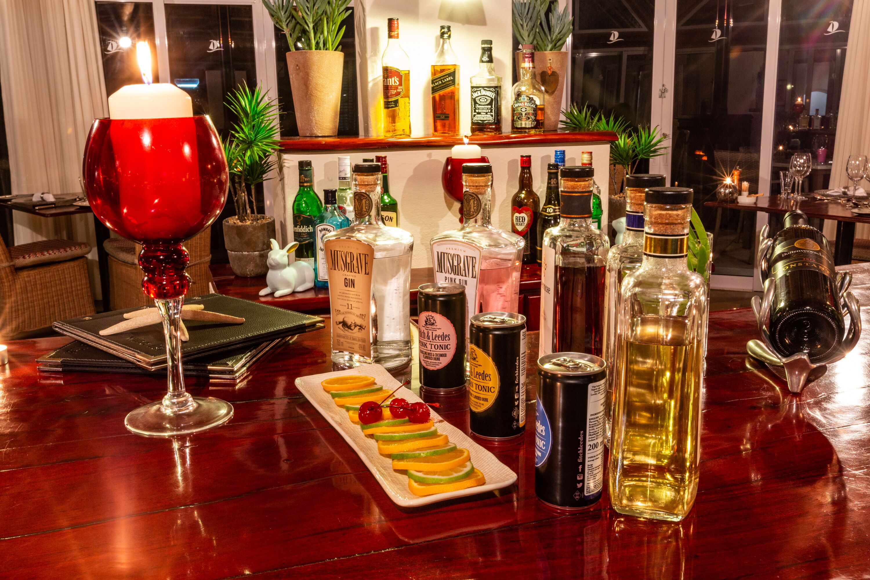 Eine Bar mit einer Auswahl an Spirituosenflaschen, einer Kerze und einem Glas Rotwein.
