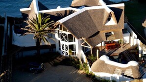A modern coastal building with a unique geometric design, featuring a large thatched roof and a pool area. - The Sands @ St Francis (Saint Francis Bay)