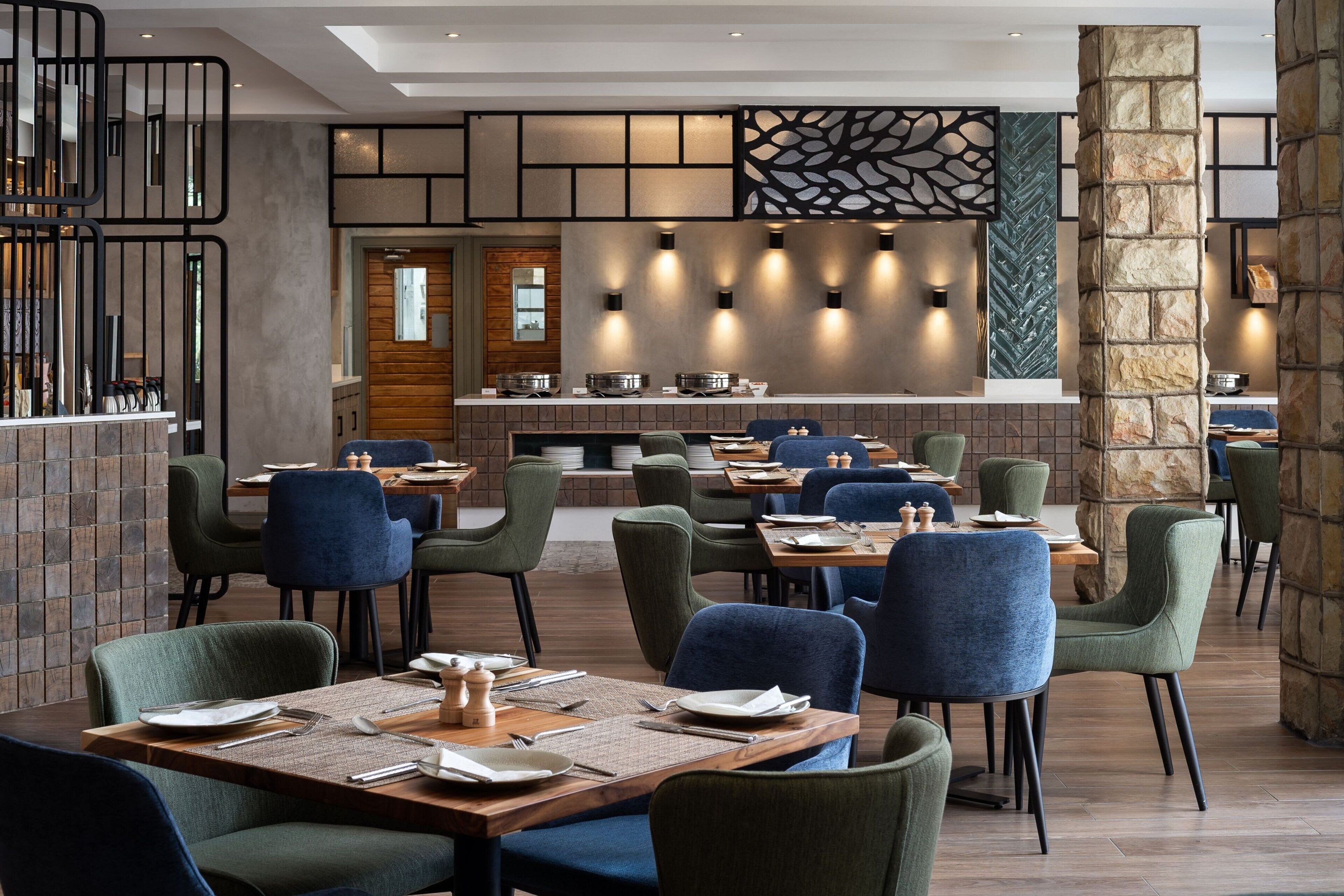 A restaurant with multiple tables and chairs, a stone pillar, and a wall with a geometric pattern.