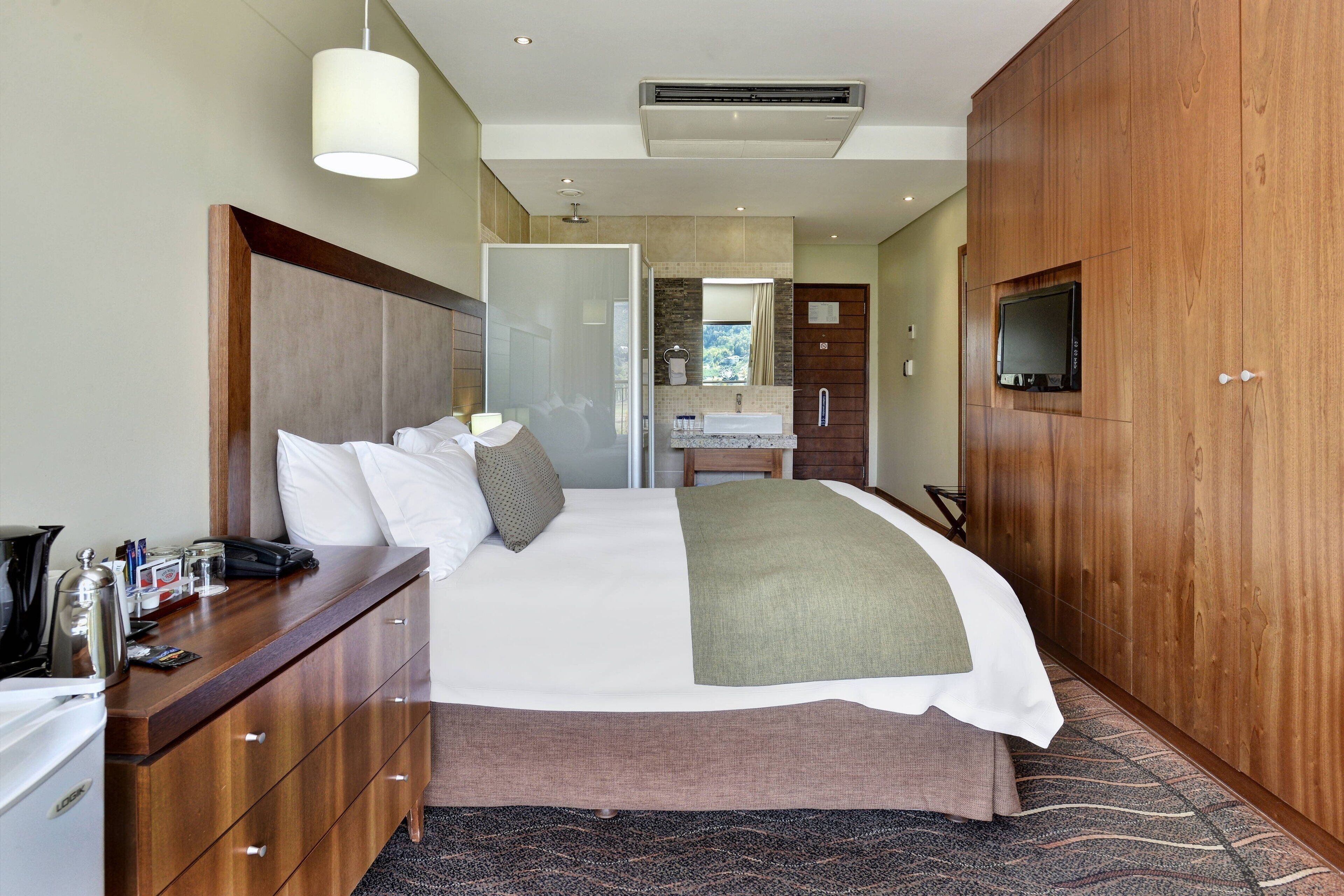 Habitación de hotel con una cama grande, armario de madera, un escritorio con teléfono y televisor montado en el armario.