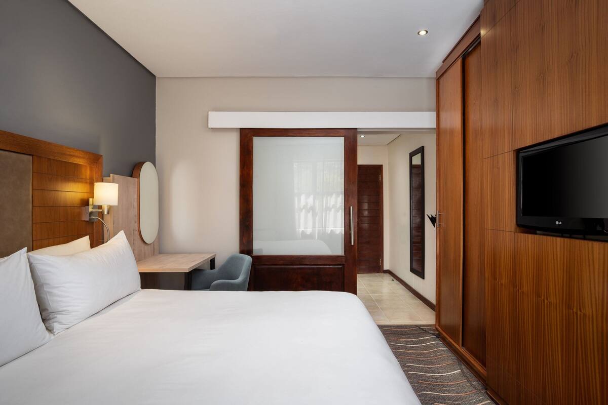 Ein Hotelzimmer mit einem großen Bett, einem Schreibtisch, einem Sessel, einem Fernseher und einem Kleiderschrank.