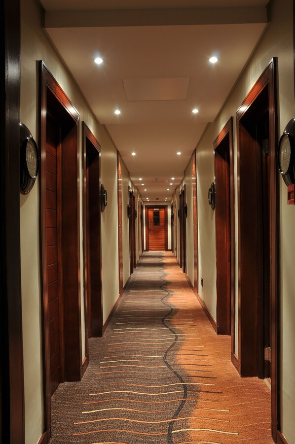 Un pasillo de hotel con puertas de madera, suelo alfombrado e iluminación empotrada en el techo.