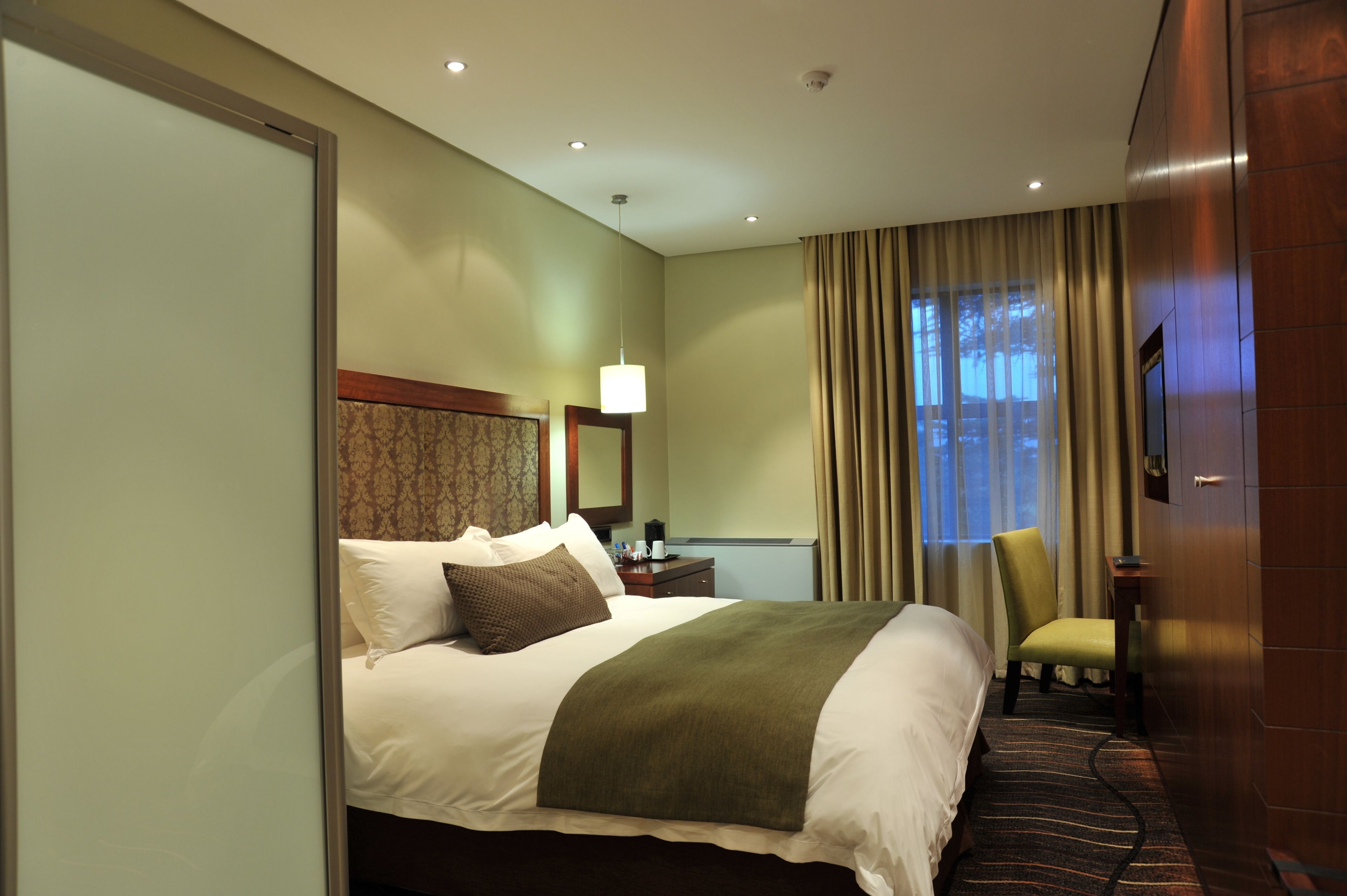 A hotel room with a bed, a chair, a desk, a lamp, and a television.