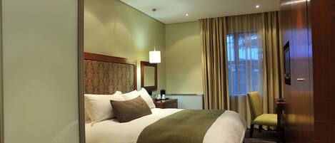 A hotel room with a bed, a chair, a desk, a lamp, and a television.