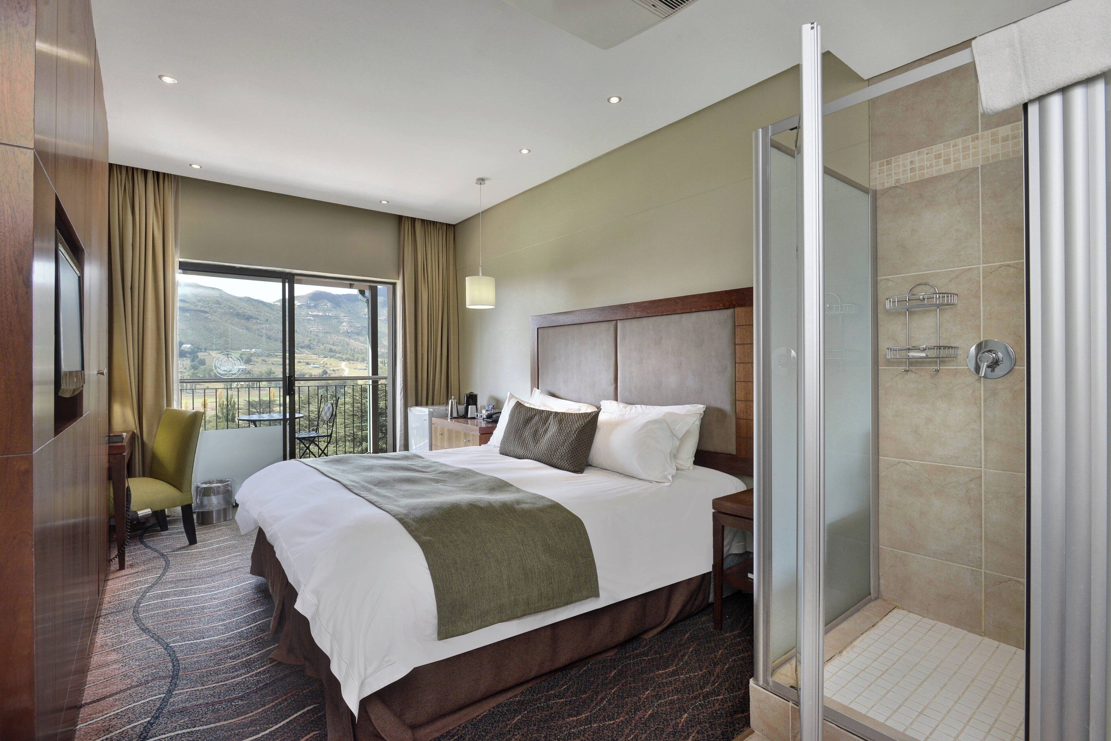 Habitación de hotel con una cama grande, ducha, vistas a la montaña y un balcón con una silla.
