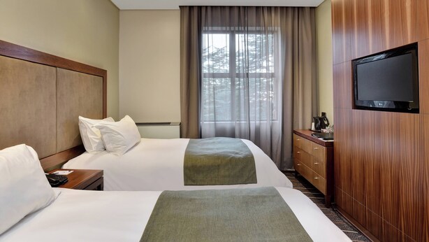 Ein Hotelzimmer mit zwei Betten, einem Holzschrank, einem Flachbildfernseher und einem Fenster mit Vorhängen.