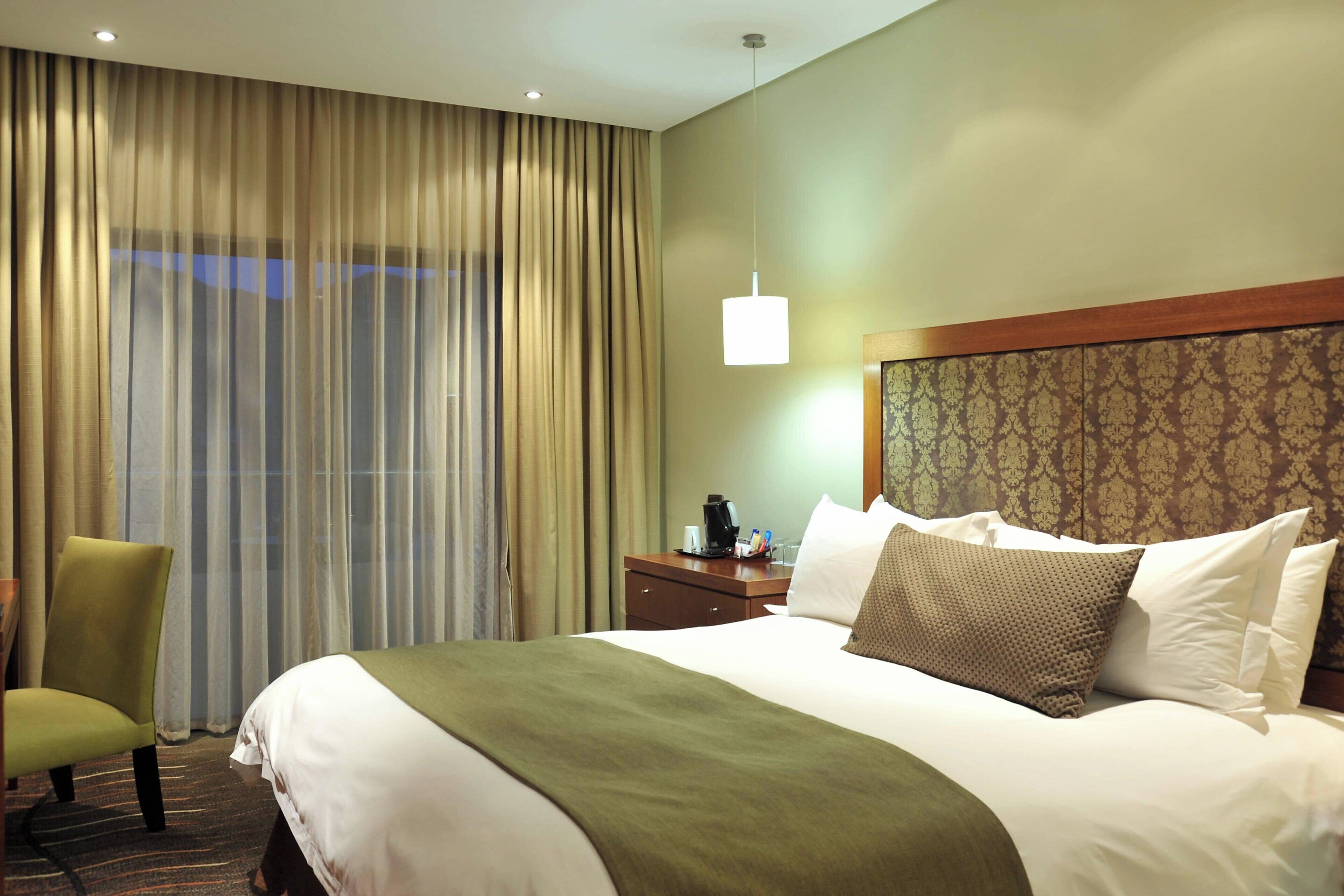 Une chambre d’hôtel avec un grand lit, une chaise, une table de chevet et une fenêtre avec des rideaux.