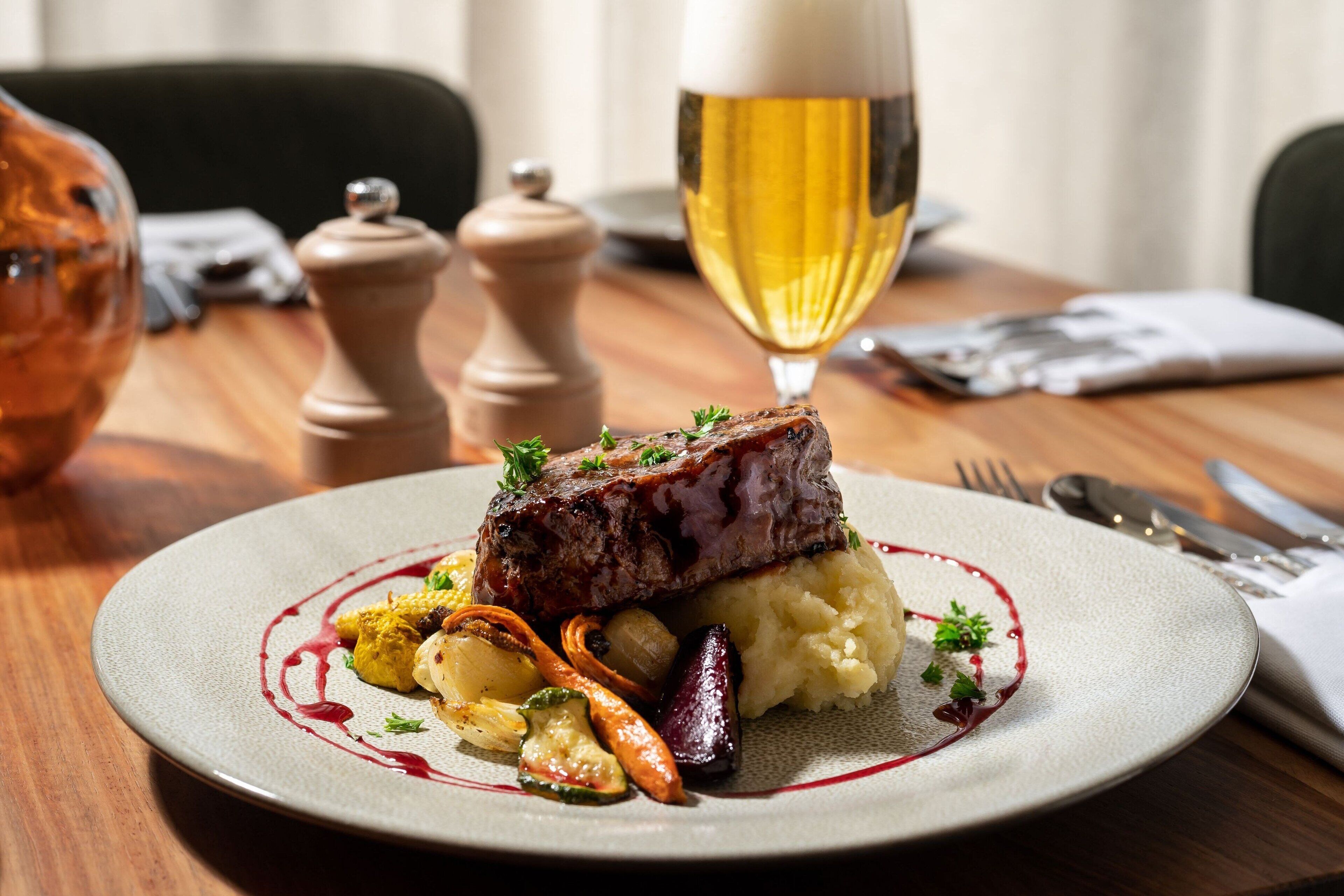 A plate of food with a steak, mashed potatoes, and vegetables, accompanied by a glass of beer.