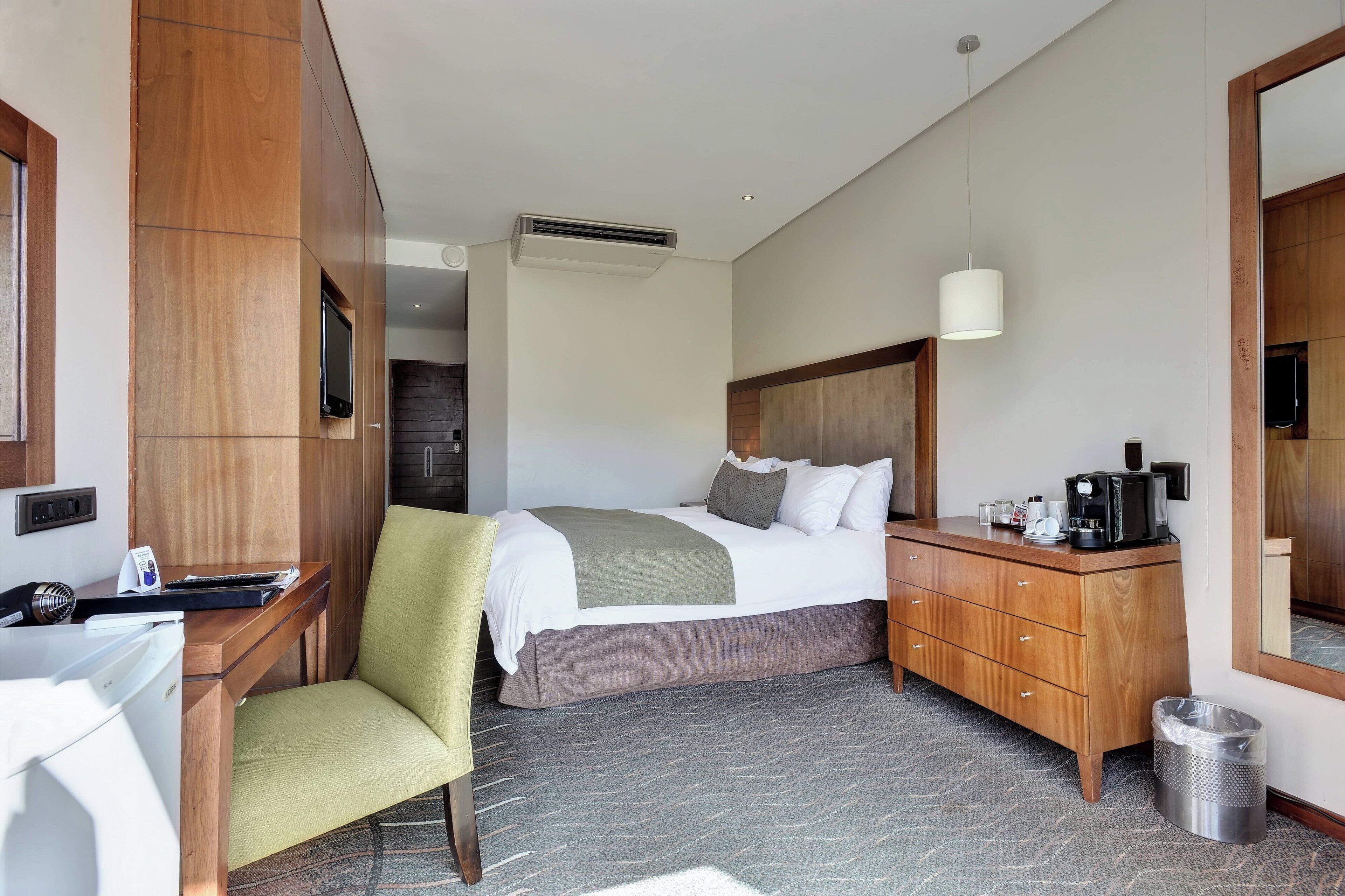 A hotel room with a bed, a desk, a chair, a dresser, a trash can, and a wall-mounted TV.