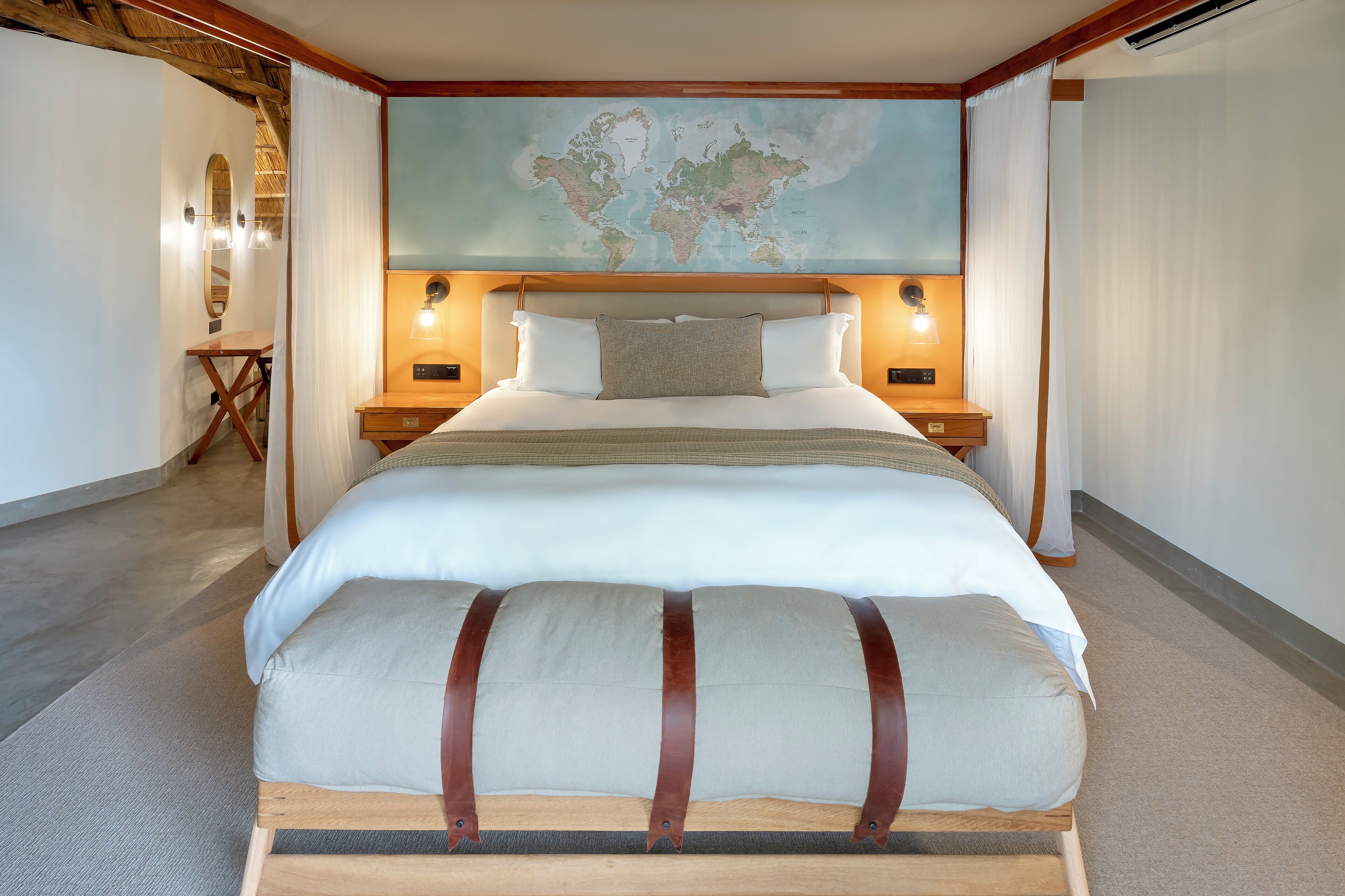 A neatly made bed with a world map above it, wooden headboard, and bedside lamps.
