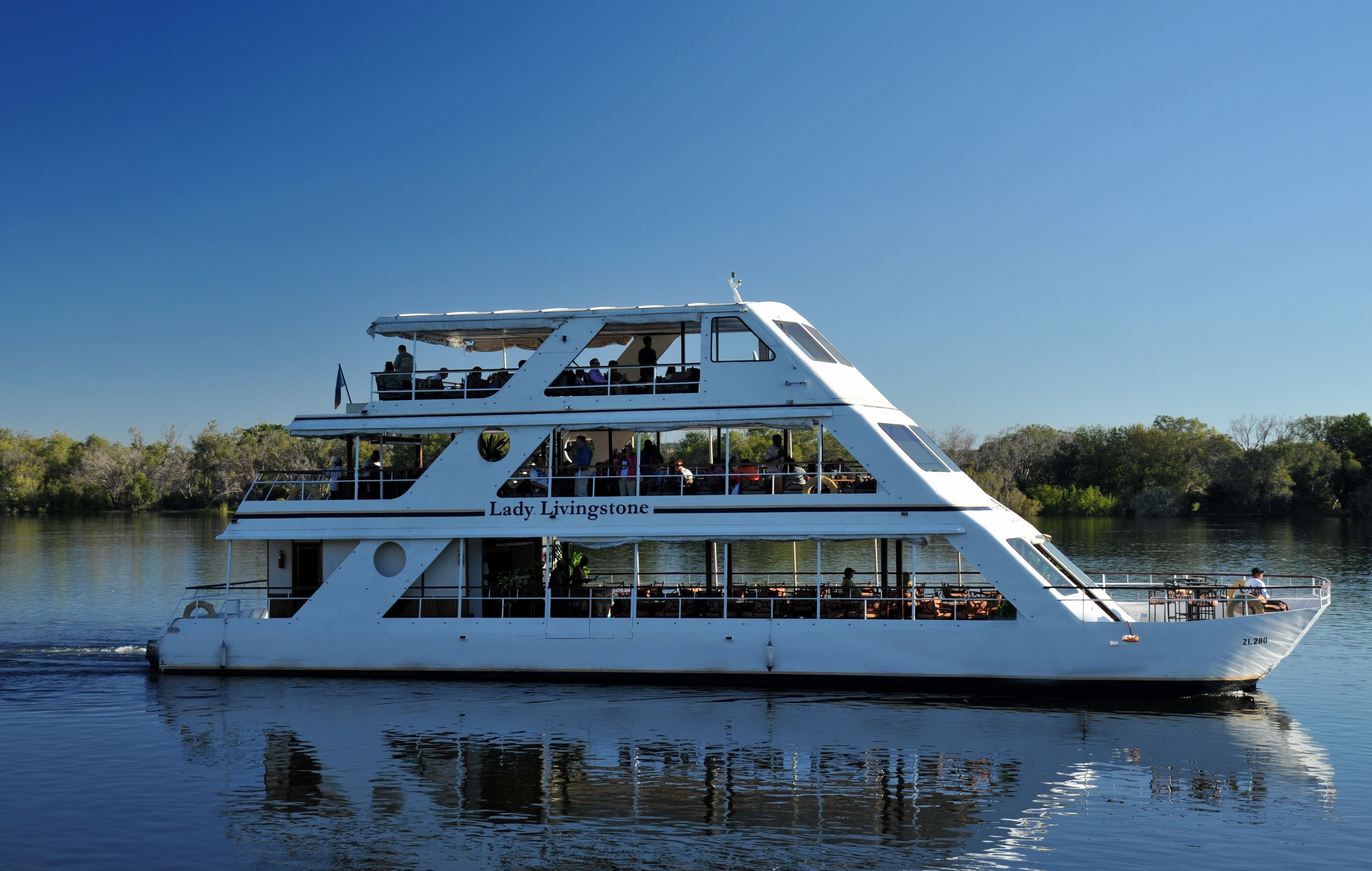 A multi-deck boat named Lady Livingstone with outdoor seating and dining areas, surrounded by calm water and greenery.