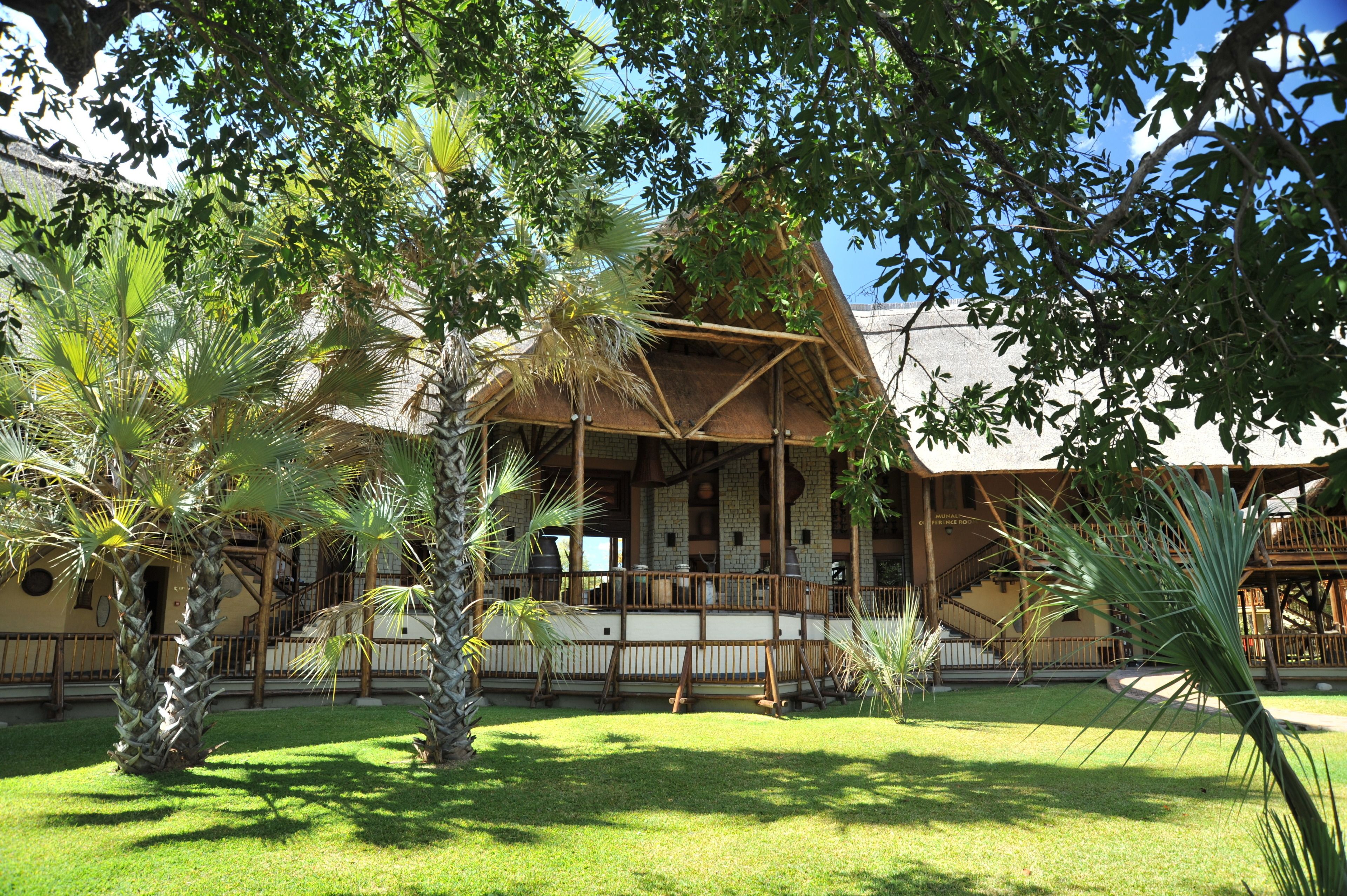 A traditional wooden building with a thatched roof, surrounded by palm trees and a well-maintained lawn.