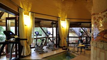 Un gimnasio con equipamiento de ejercicio, piscina y ventanas grandes con cortinas.