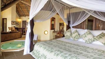 A bedroom with a canopy bed, a sitting area with a sofa and chairs, a small pool, and a bathroom with a mirror and sink.