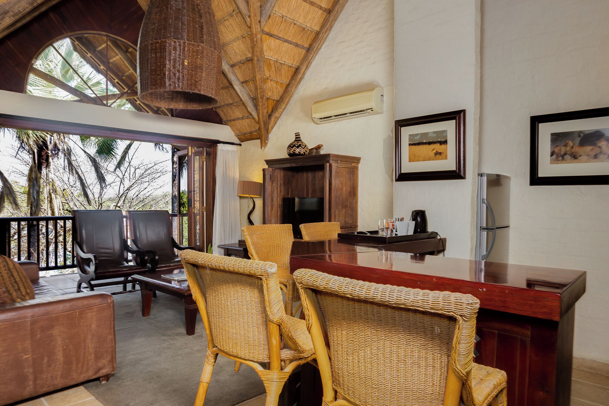 A spacious room with a high ceiling, a large dining table, wicker chairs, a bar area, and a television.