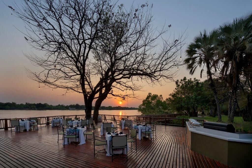 A sunset view from a deck with tables set for dining, overlooking a body of water.