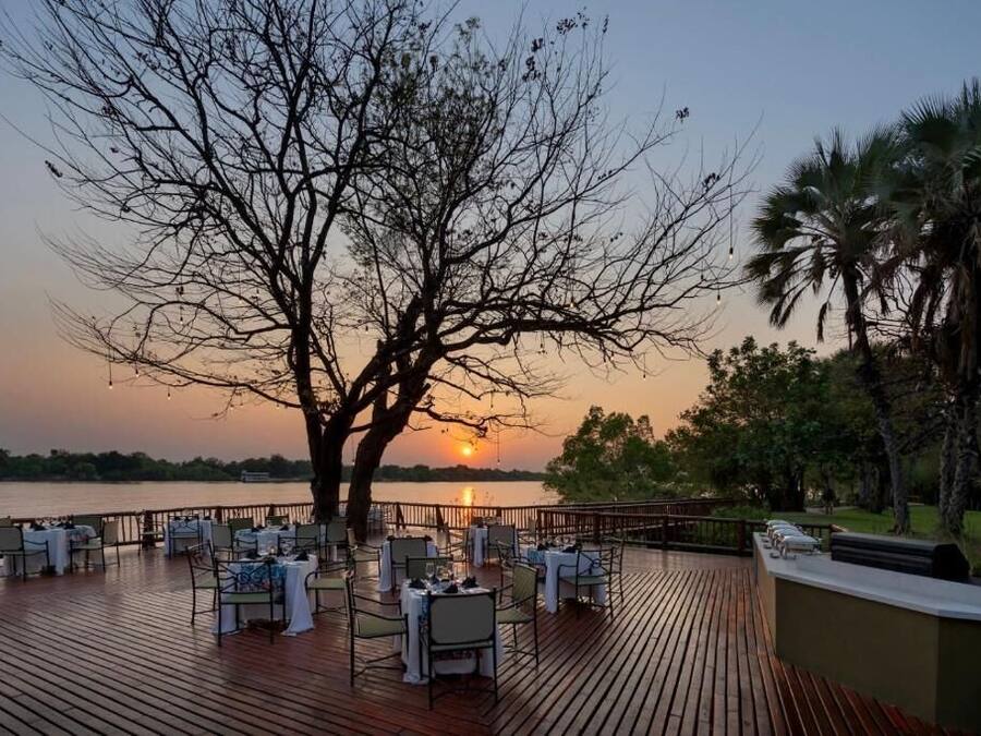 A sunset view from a deck with tables set for dining, overlooking a body of water.