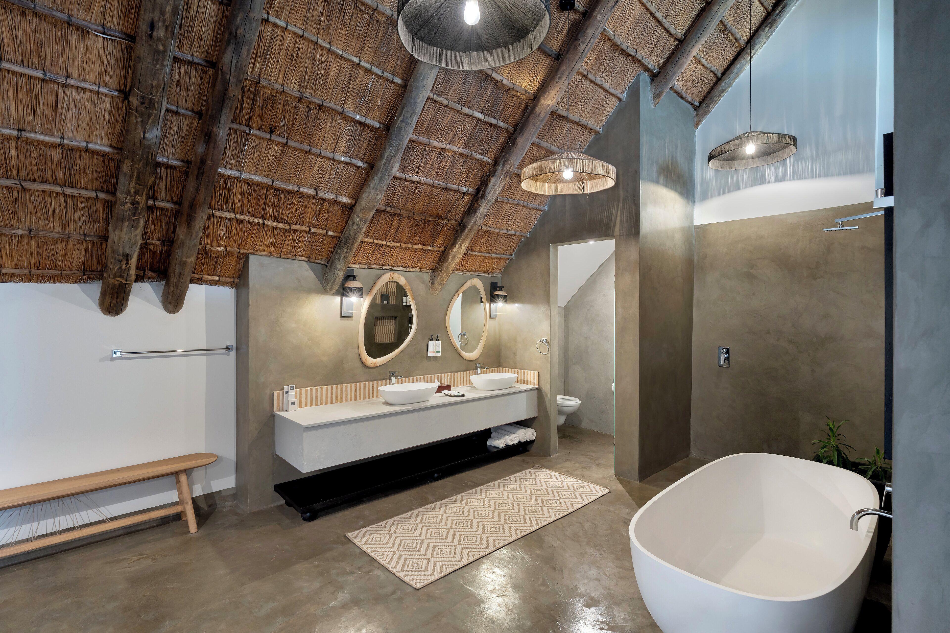 A modern bathroom with a large bathtub, a vanity with two sinks, and a bench.