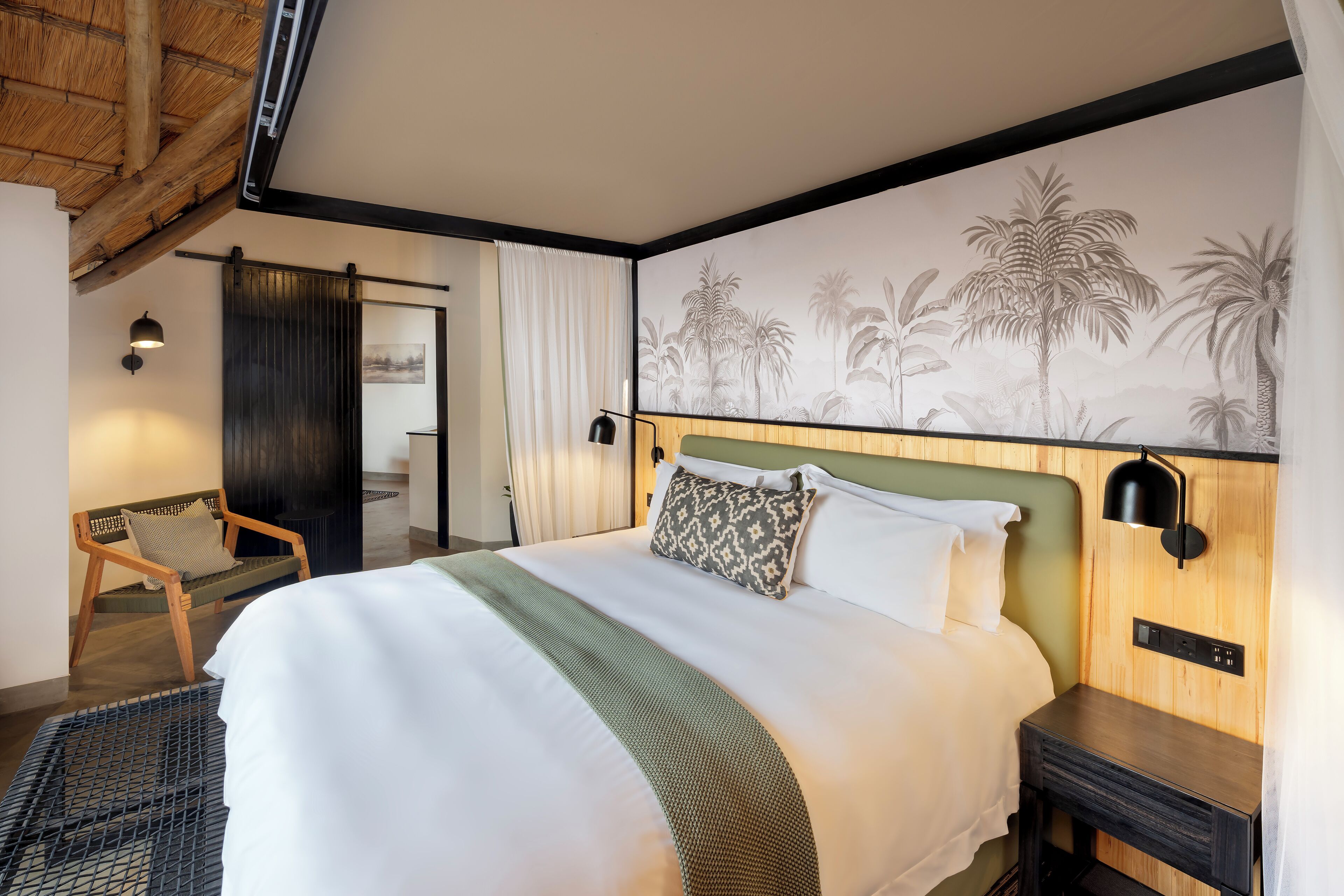 A neatly arranged bedroom with a large bed, a wooden headboard, a nightstand, a chair, and a wall mural.
