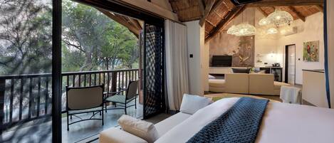 A modern hotel room with a large bed, a balcony with seating, and a dining area.