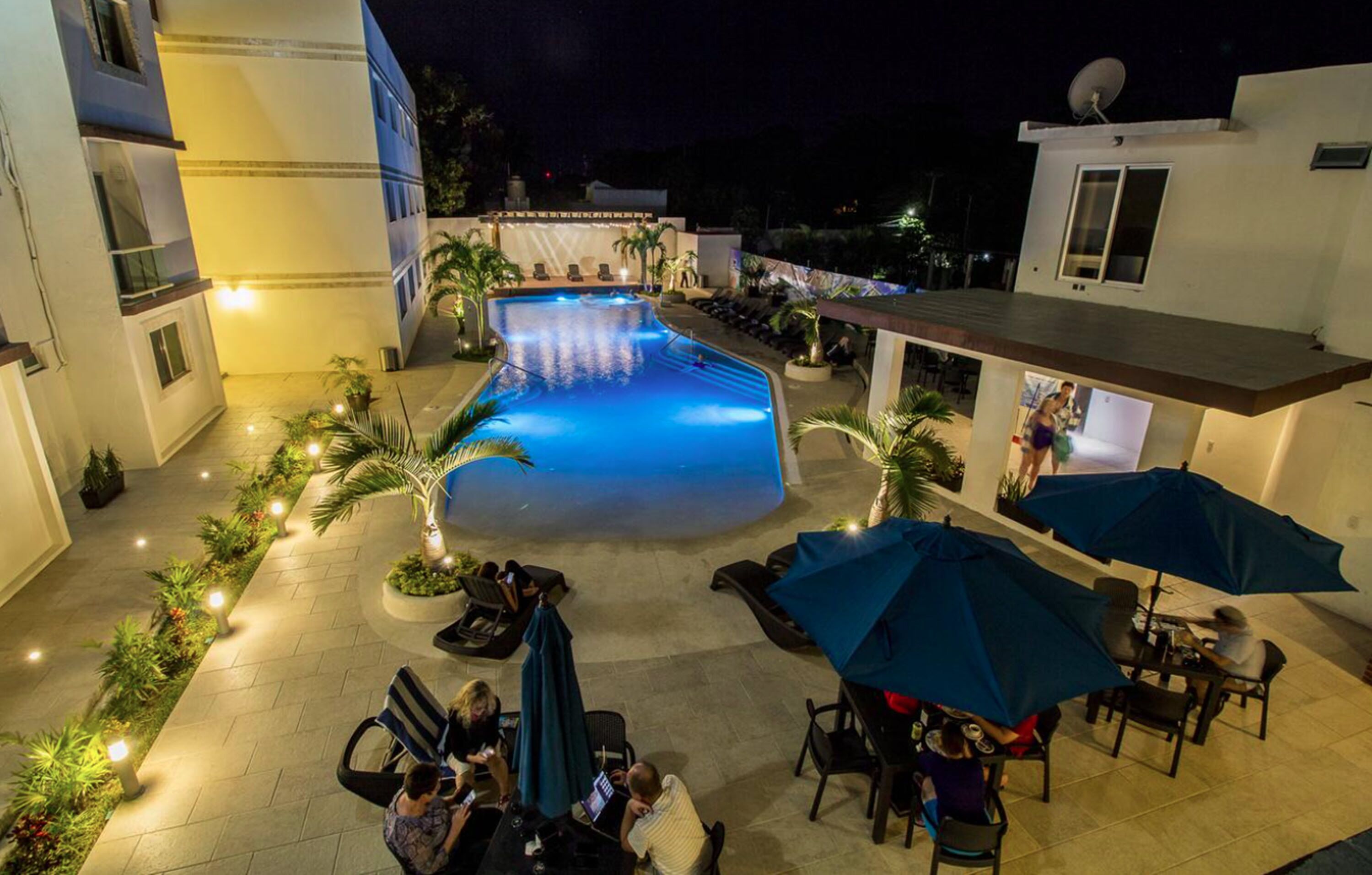A swimming pool surrounded by lounge chairs and umbrellas, with a building in the background.