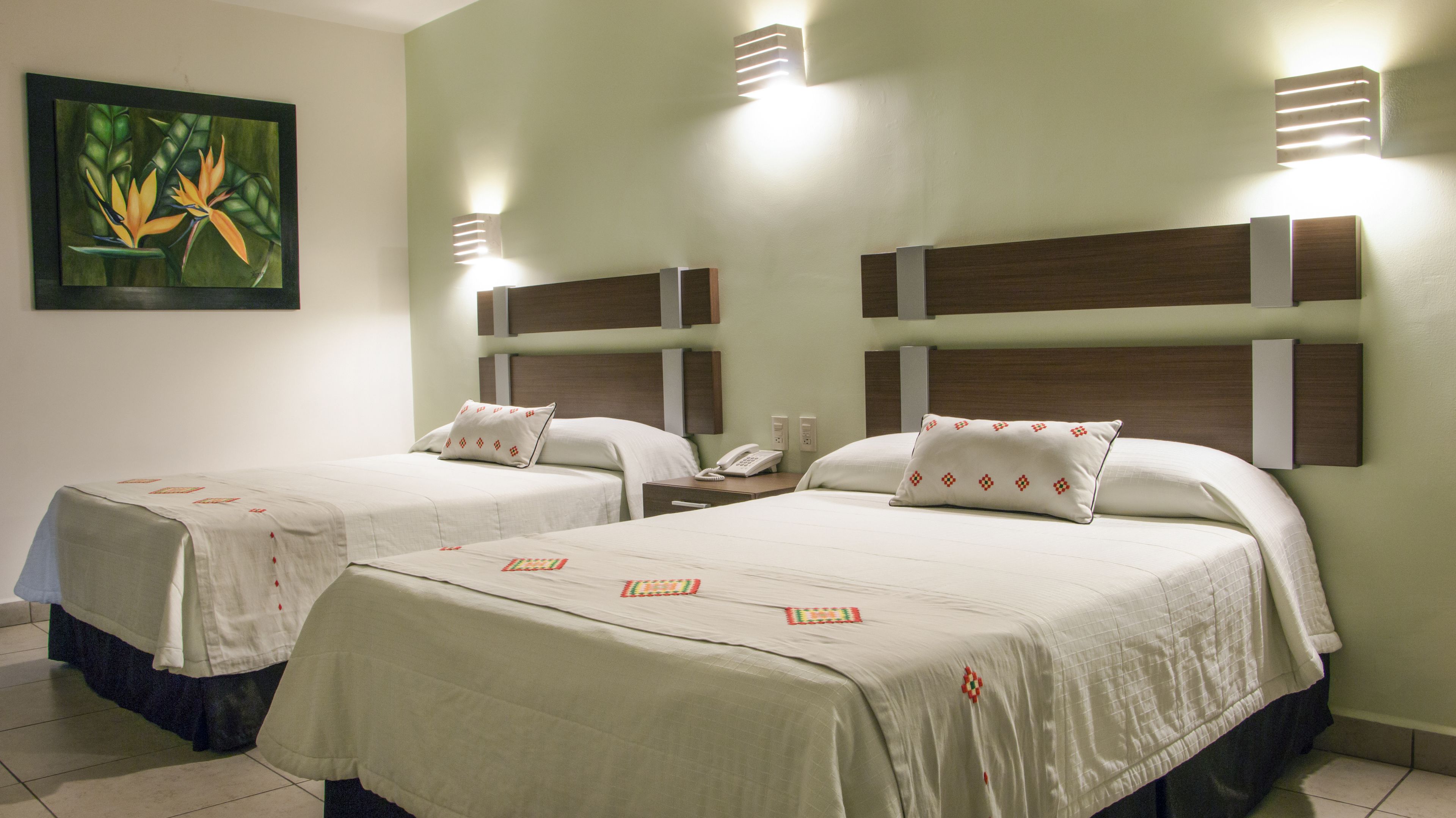 Ein Hotelzimmer mit zwei Betten, einem Wandbild mit tropischen Blumen und moderner Wandbeleuchtung.