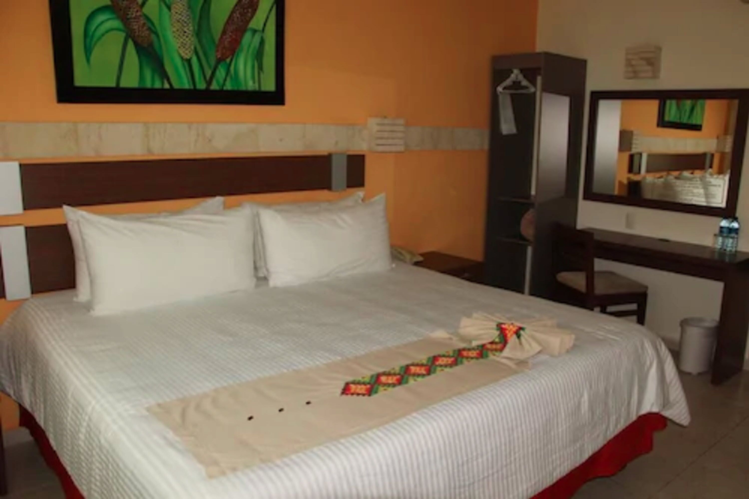 A hotel room with a bed, a desk, a mirror, and a painting on the wall.