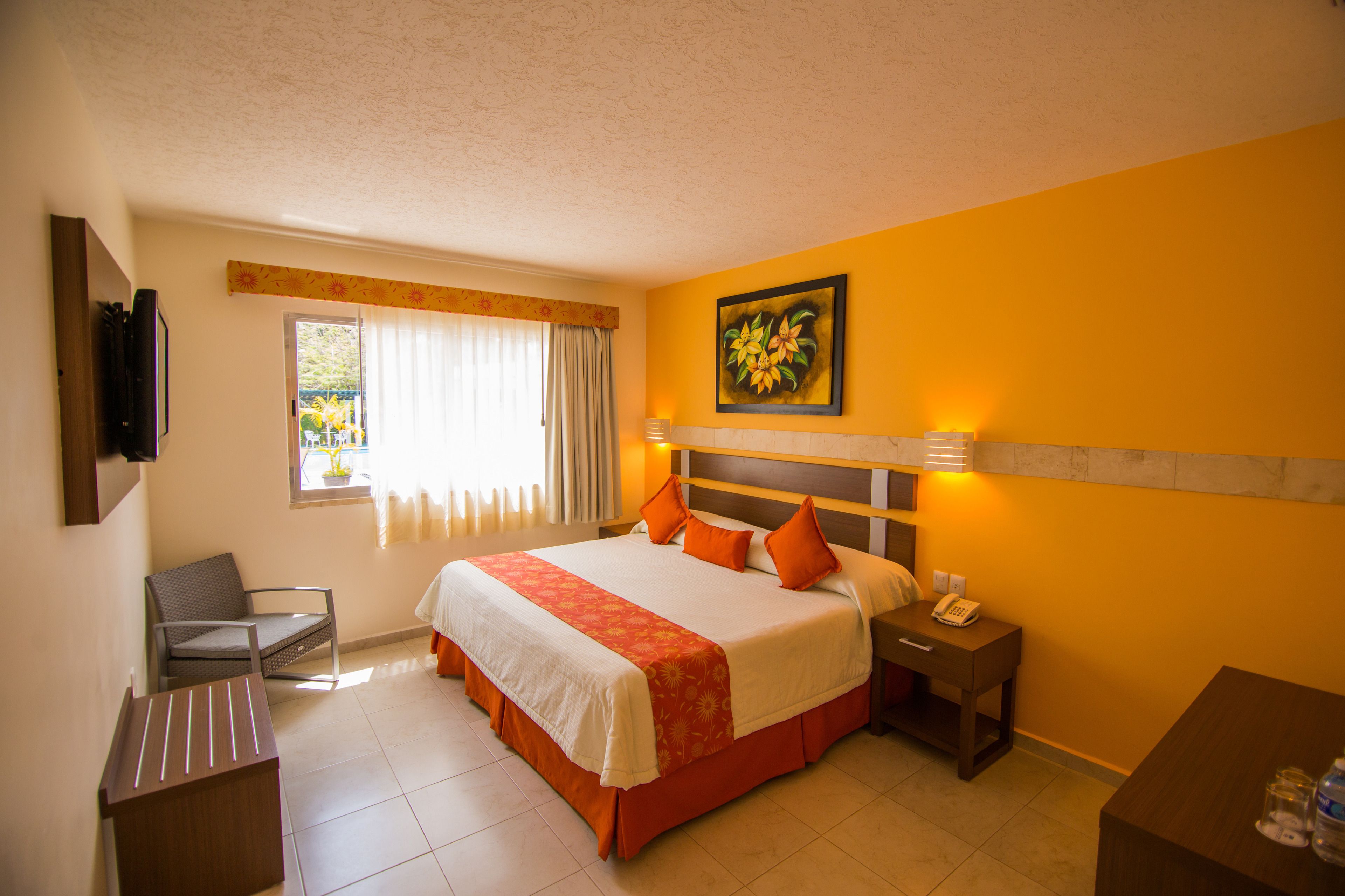 A hotel room with a bed, a chair, a desk, a nightstand, and a painting on the wall.