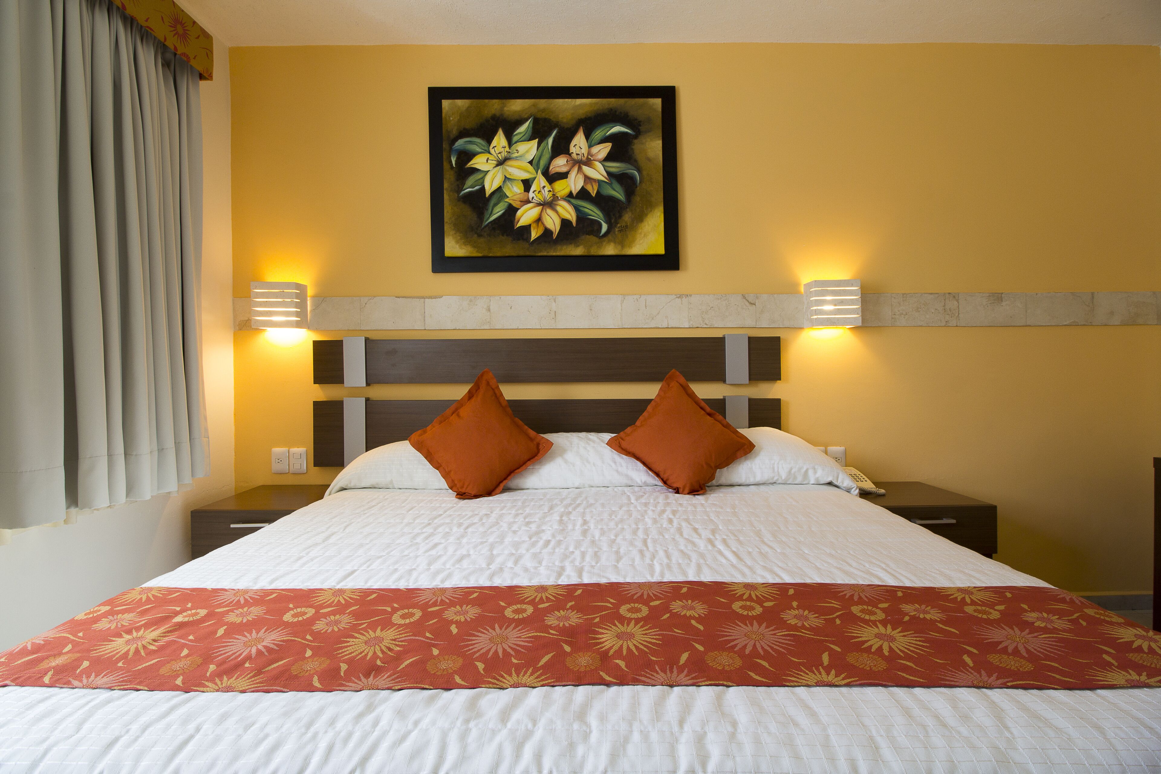 Habitación de hotel con cama, dos almohadas, mesita de noche, lámpara y un cuadro en la pared.