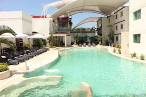 A swimming pool with lounge chairs and umbrellas, surrounded by buildings with balconies.